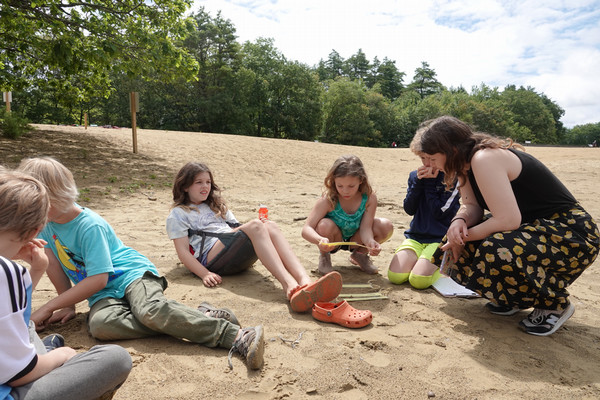 Shoshi leans over to interact with five kids on a beach.