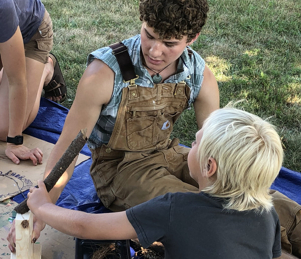 Kyle sits with a child, holding a stick.