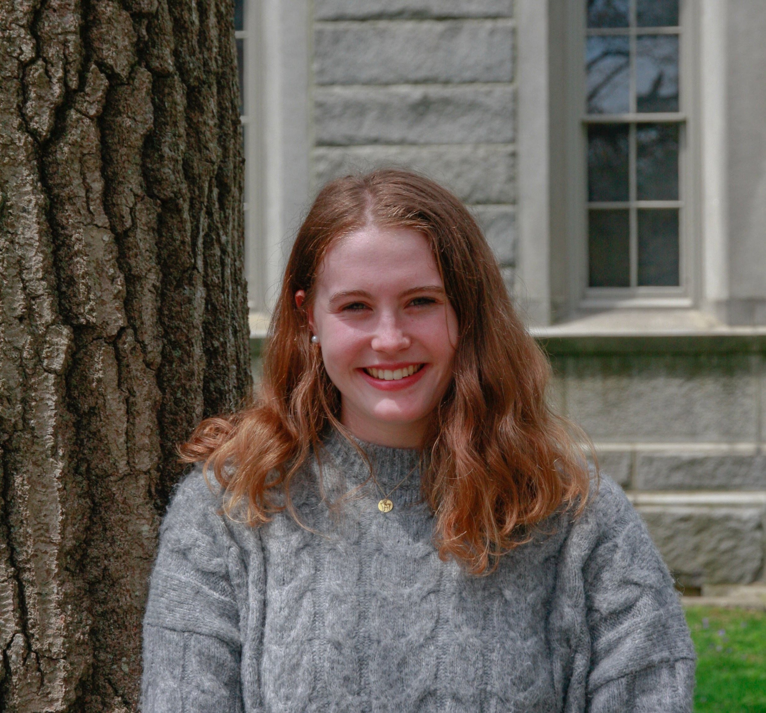 Ruby, wearing a grey sweater, smiles at the camera. 