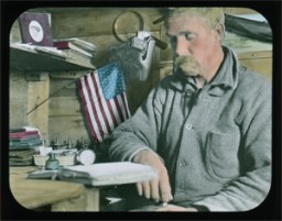 Harrison Hunt, expedition surgeon and Bowdoin Class of 1902, reading at a desk in the expedition’s headquarters. Note the pile of field notebooks and journals on the desk. Hand-tinted glass lantern slide, Northwest Greenland, 1913-17. Elmer Ekblaw Collection. Given in honor of Walter E. Ekblaw, Jr., devoted son.
