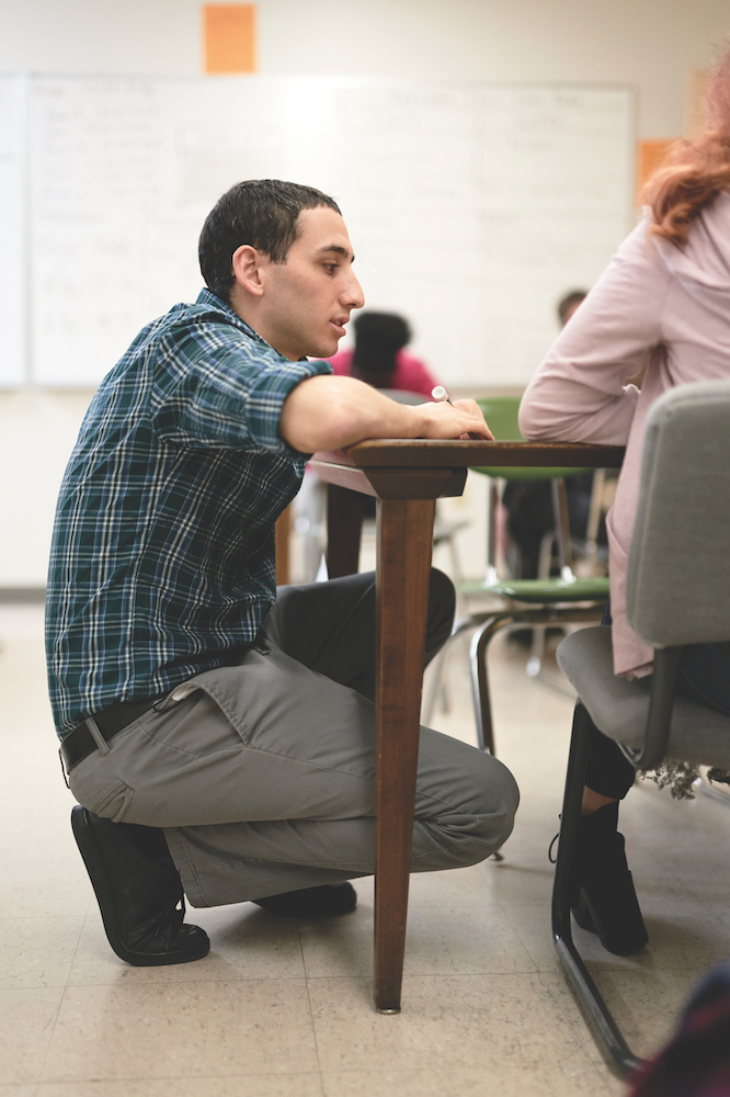 Matt Bernstein ’13 kneels to look onto the work of one of his students.