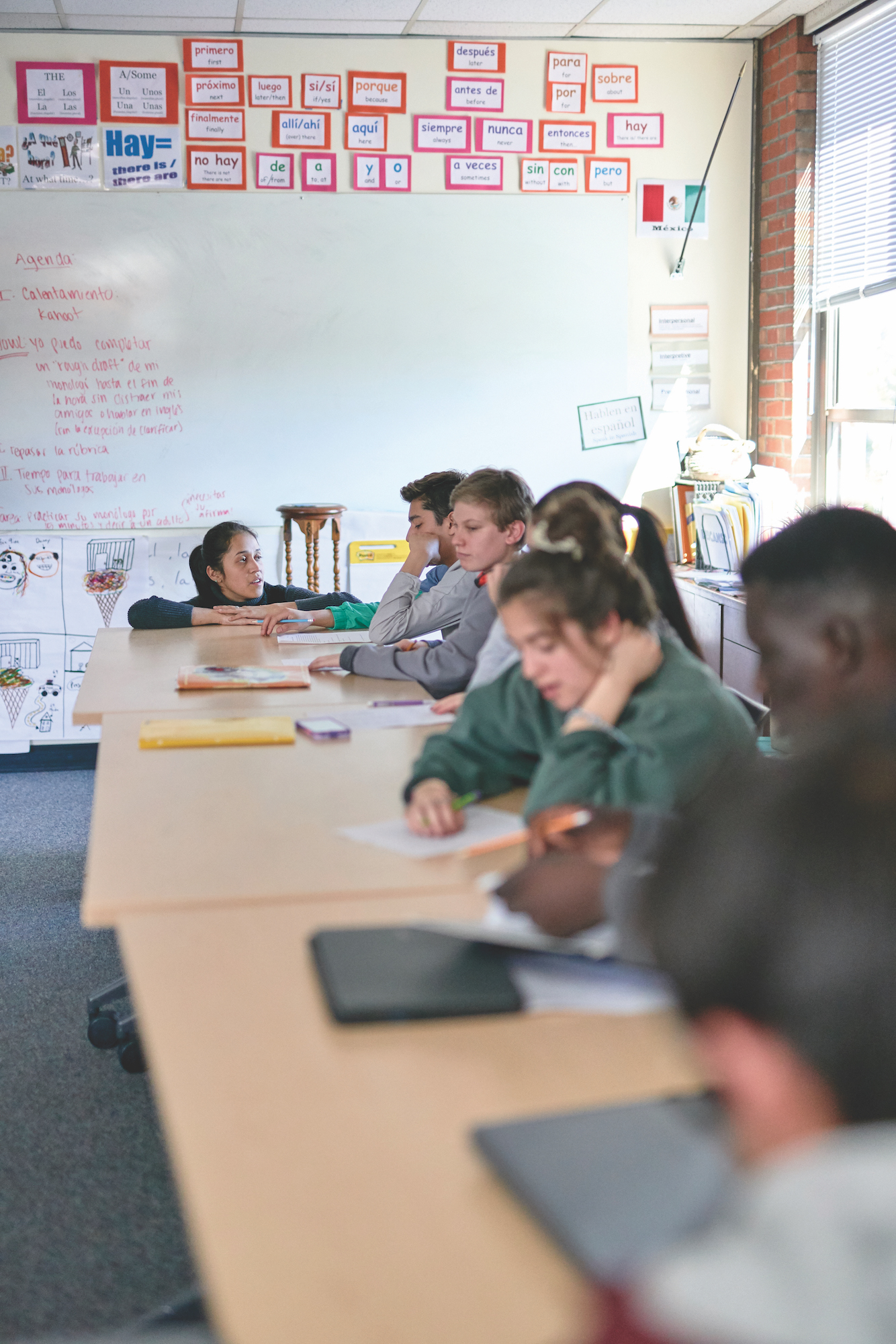 Angela Wunderlich ’19 is in a Spanish classroom at Casco Bay Highschool kneeling down talking to one of her students.