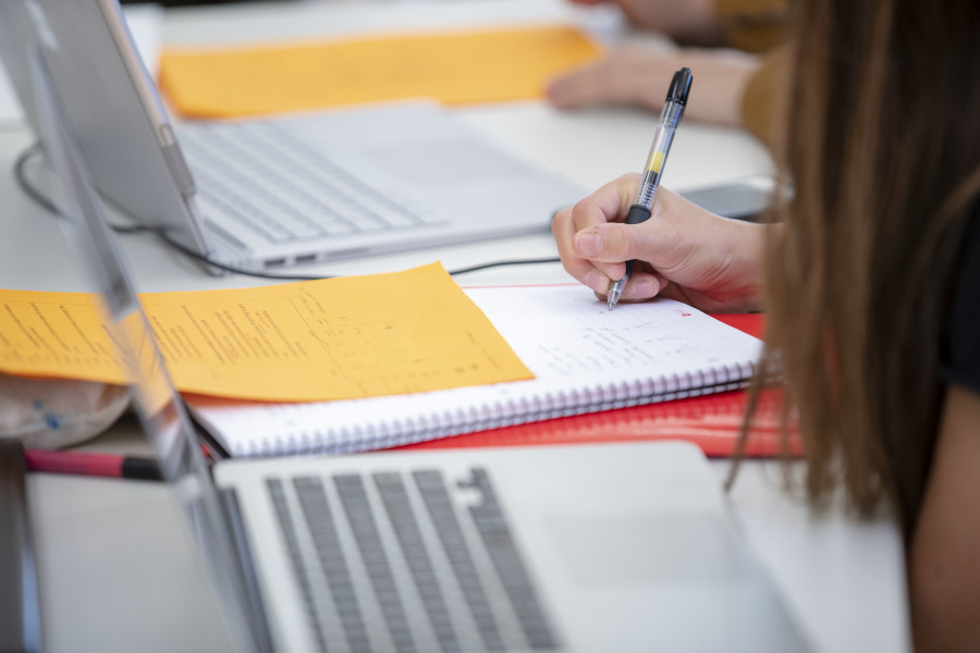 Student writing in a notebook surrounded by computers