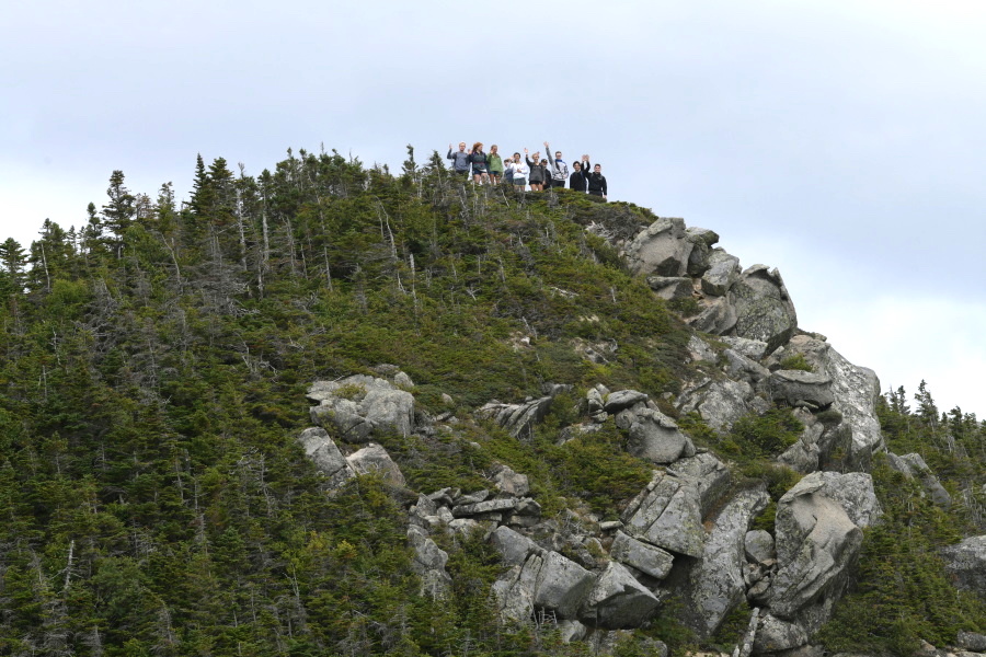 The group of students wave from a rocky knoll