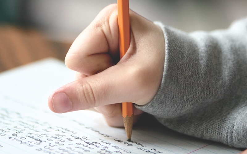 Student clenching a pencil, forcing the skin between their thumb and index finger back, so they can increase the pressure their pencil has on the paper.