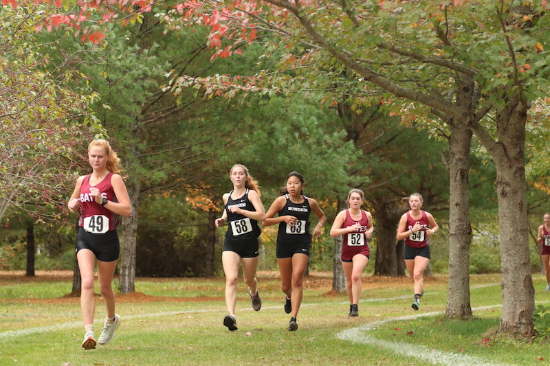 Two Bowdoin runners at a home meet running under colorful autumn leavesOct. 23.