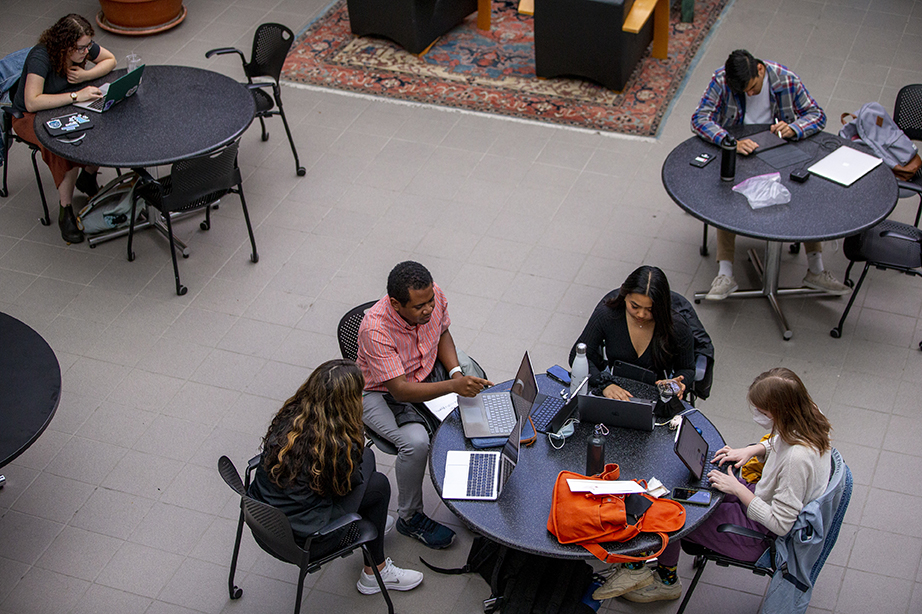 Students sitting at round tables in the Smith Student Union building, talking and doing work together. The shot is from a high angle, looking down on the students from a balcony.