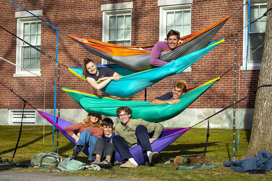 Six students in hammocks hung up on the main quad. They are smiling at the camera, with one student lying in each of the top three hammocks and three students sitting side-by-side on the bottom hammock.