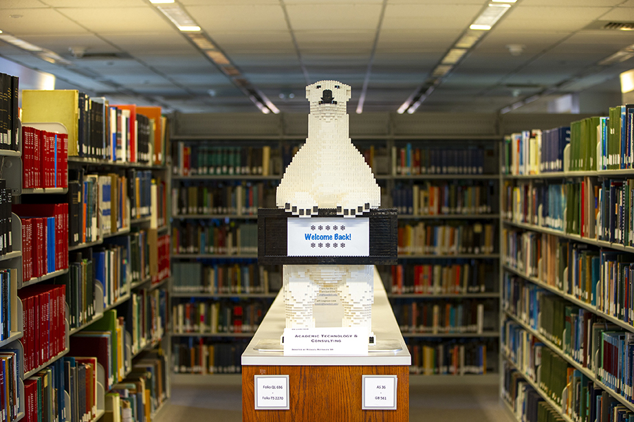 A display between two library bookshelves. The display is a polar bear made of Legos above a sign that reads "Welcome Back!"