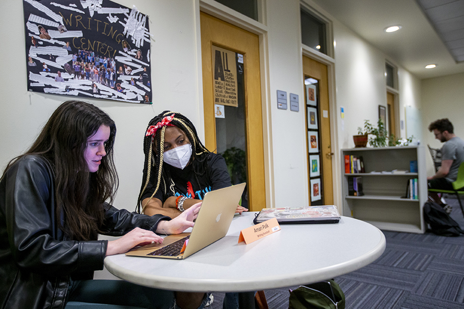 Two students sitting in the Writing Center, looking at a laptop between them.