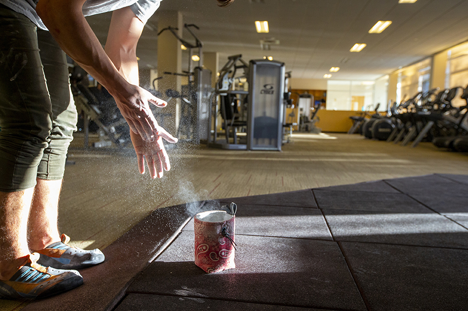 A student spreading chalk over their hands in preparation for rock climbing in the Buck Center. The light from the window shows the chalk powder suspended in the air.