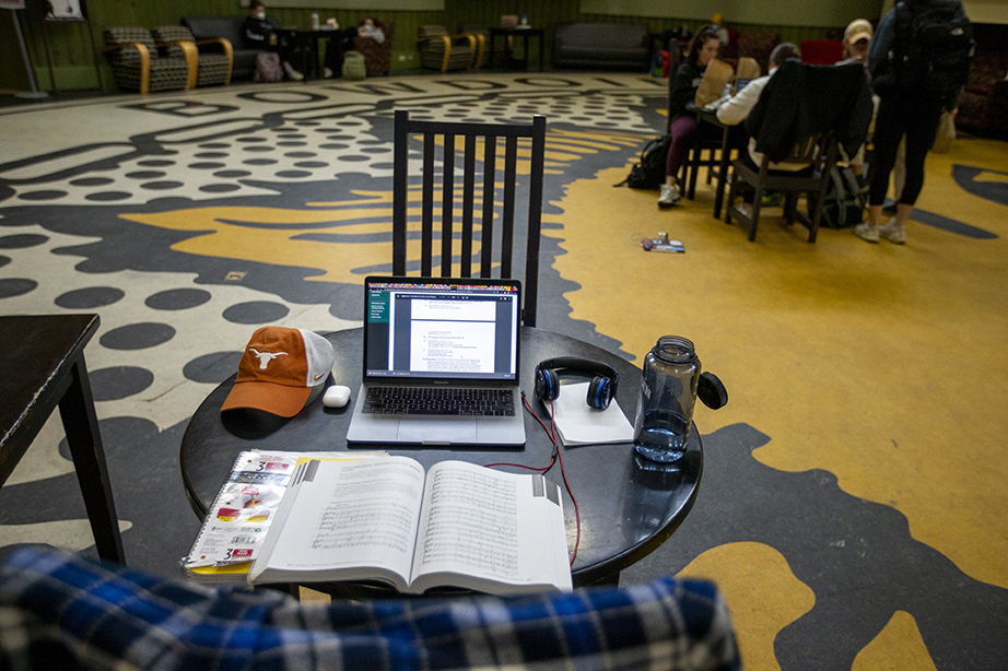 A textbook, hat, laptop, and water bottle spread out on a table in Smith Union. The picture is taken from directly behind a chair placed in front of the materials spread out on the table.