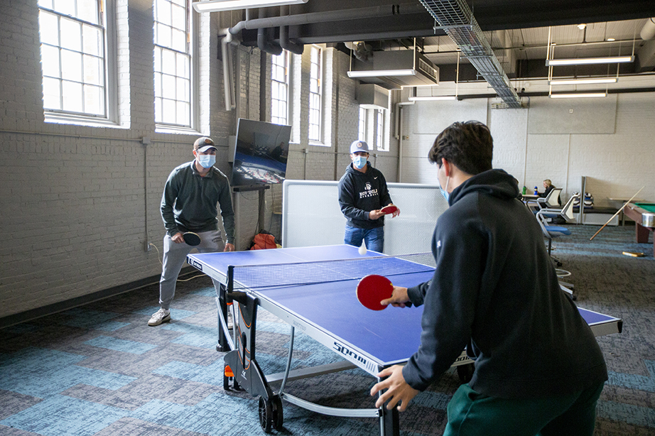Two students playing ping pong in the Smith Union game room while another student watches.
