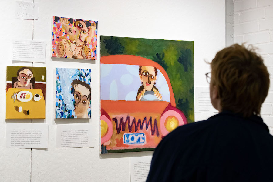 A student with glasses looks at paintings of a student with big, lopsided eyes