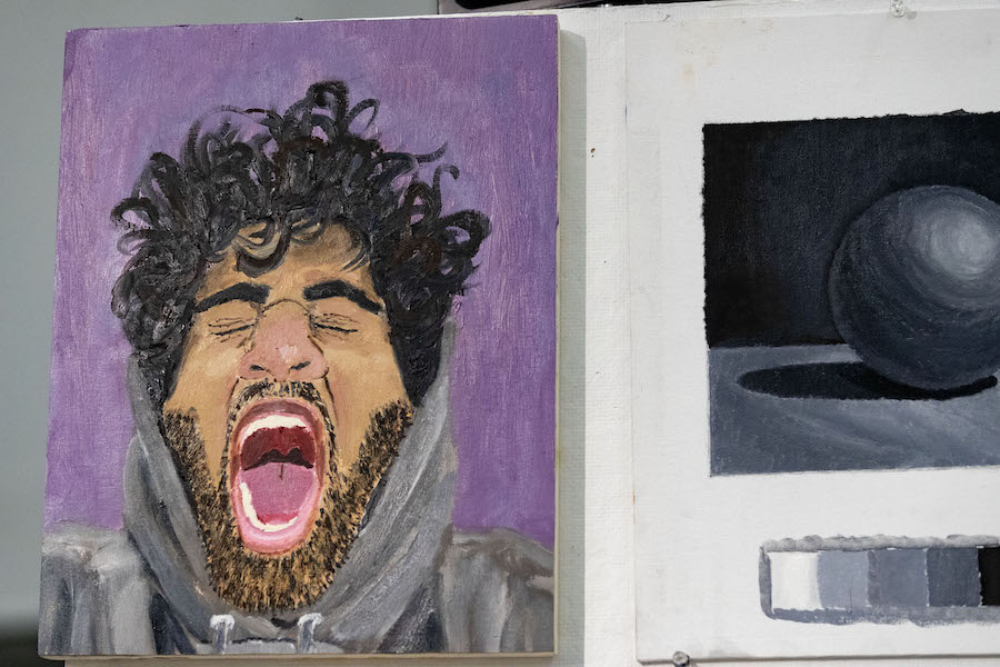 A painting of a bearded student with black curly hair and in a hoodie yawning