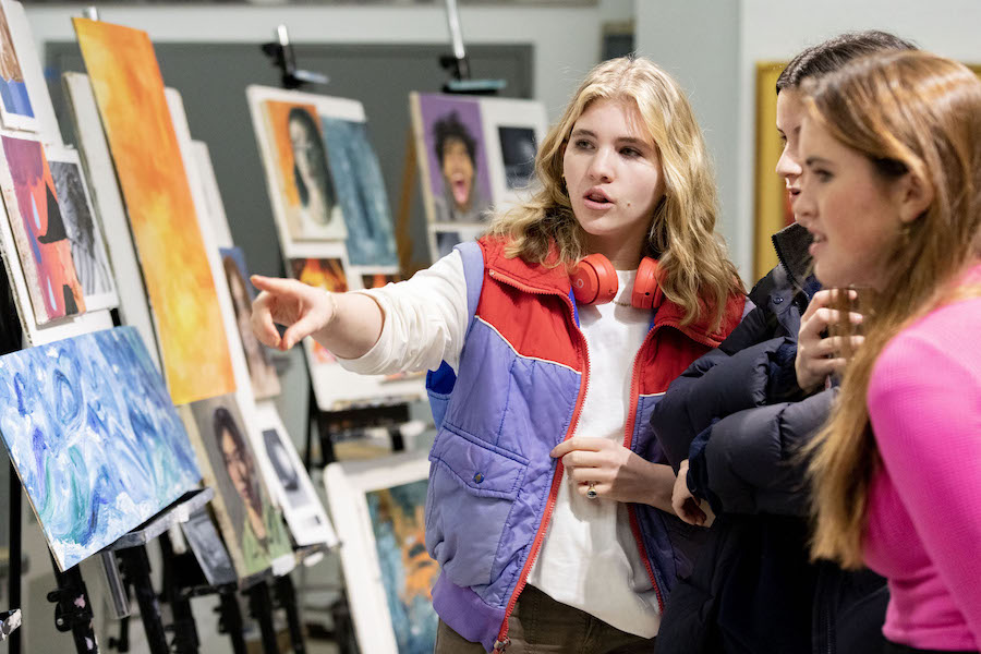 A female student with two onlookers points at a painting