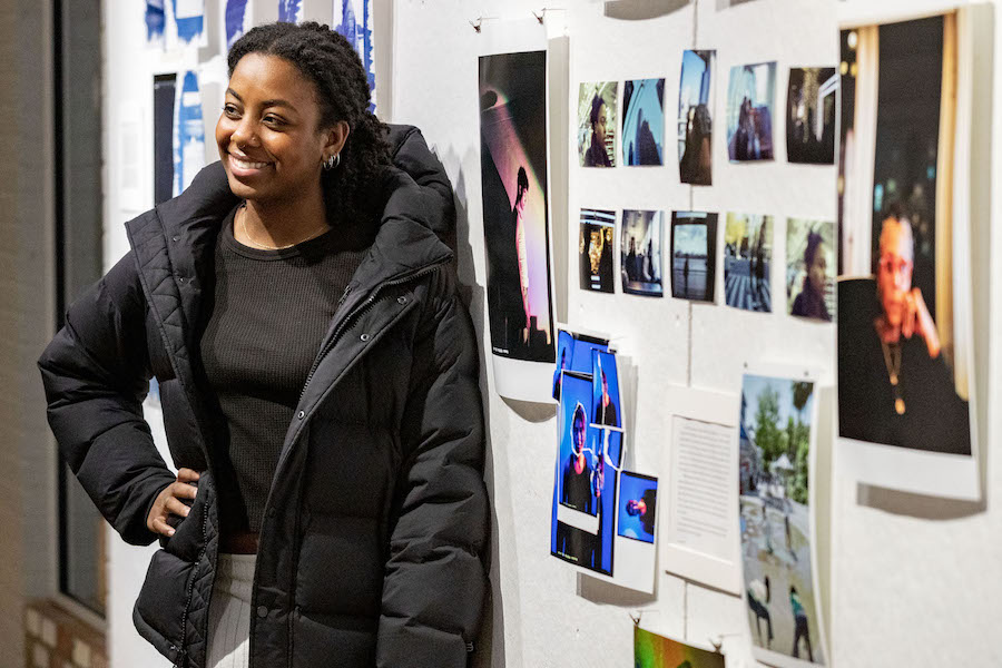 A female student poses in front of artworks on the wall