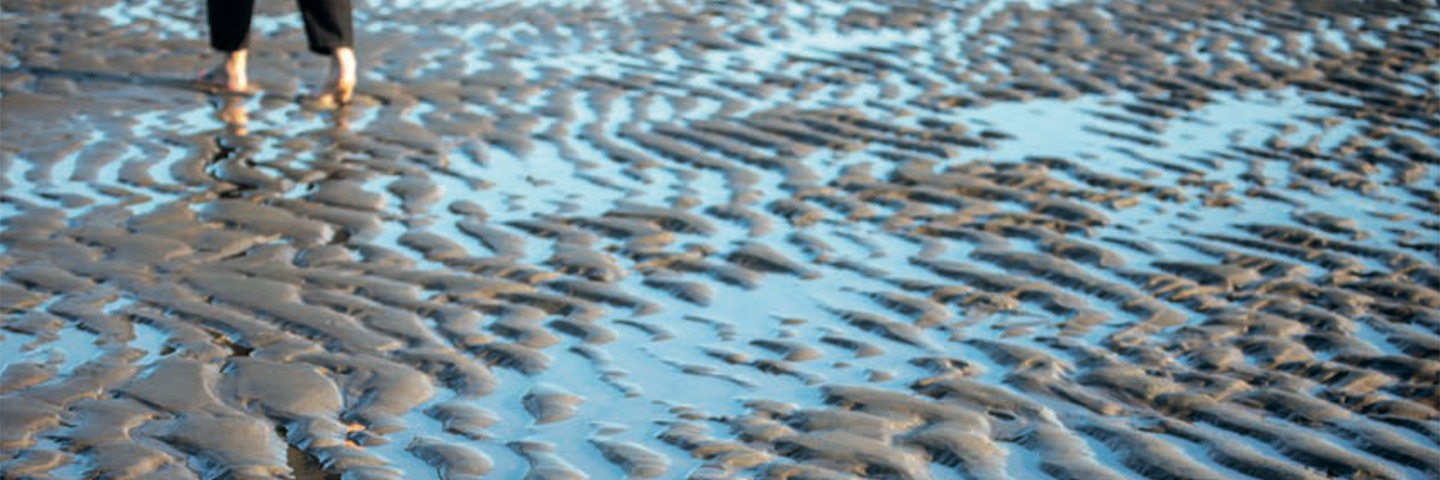 Bare feet walking in the ripples of a receding tide.