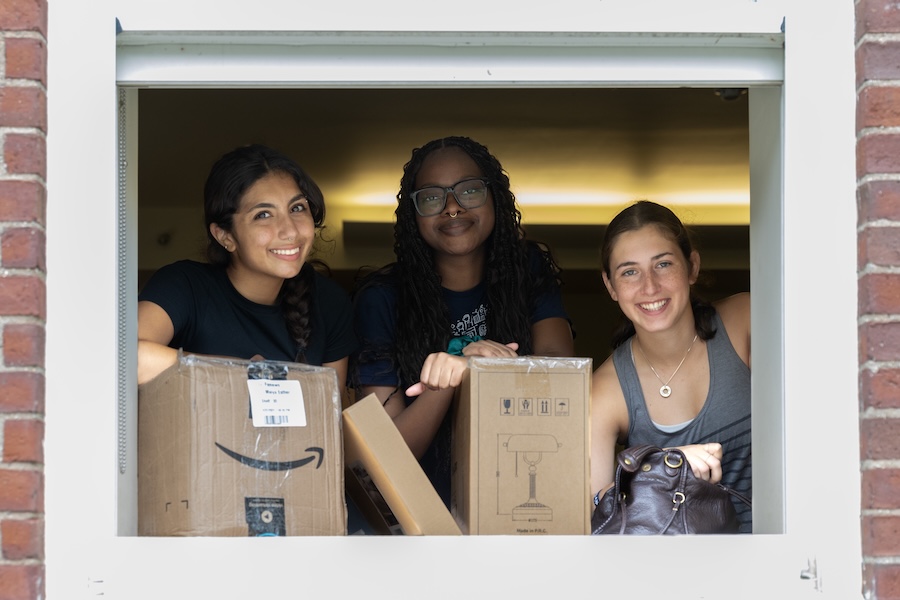 Three students in a dorm window with cardboard boxes