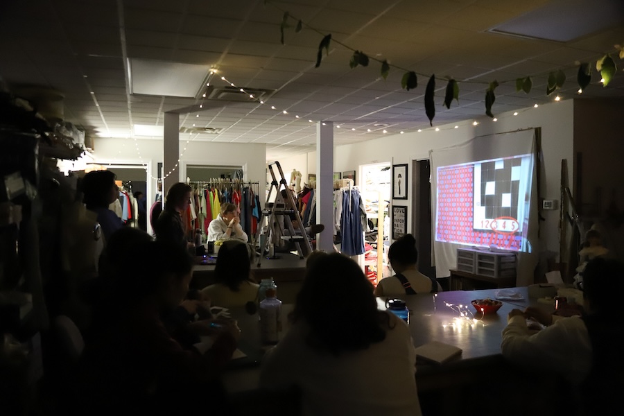 The class dims the lights to listen to a student give a presentation on satin. Here's he's explaining its weft and warp.
