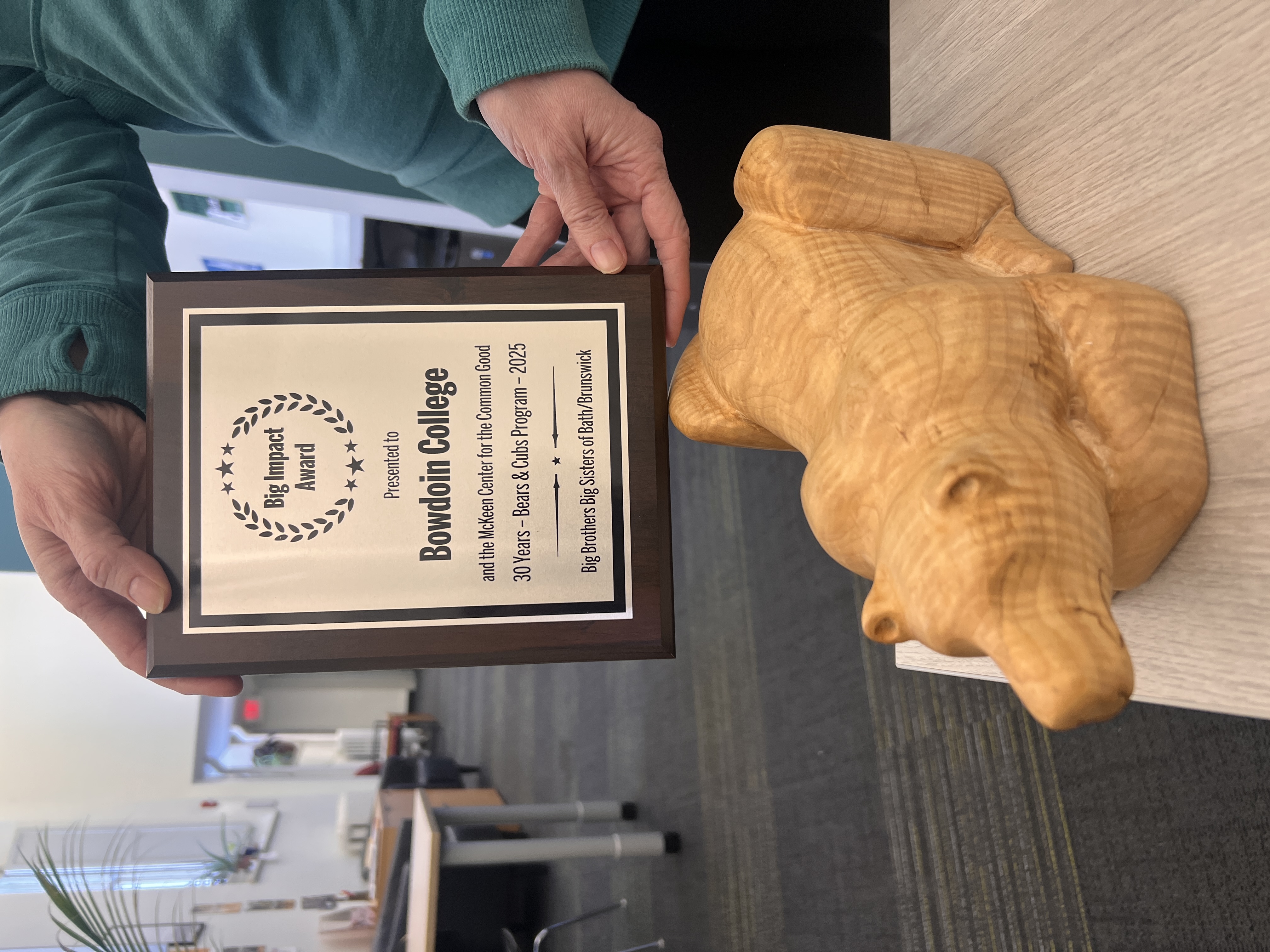 An award plaque reading: "Big Impact Award presented to Bowdoin College and the McKeen Center for the Common Good, 30 Years - Bears & Cubs Program - 2025, Big Brothers Big Sisters of Bath/Brunswick". The plaque is being held above a carved wooden statuette of a polar bear.