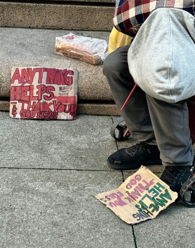 A man sits next to a sign that says "Anything Helps"