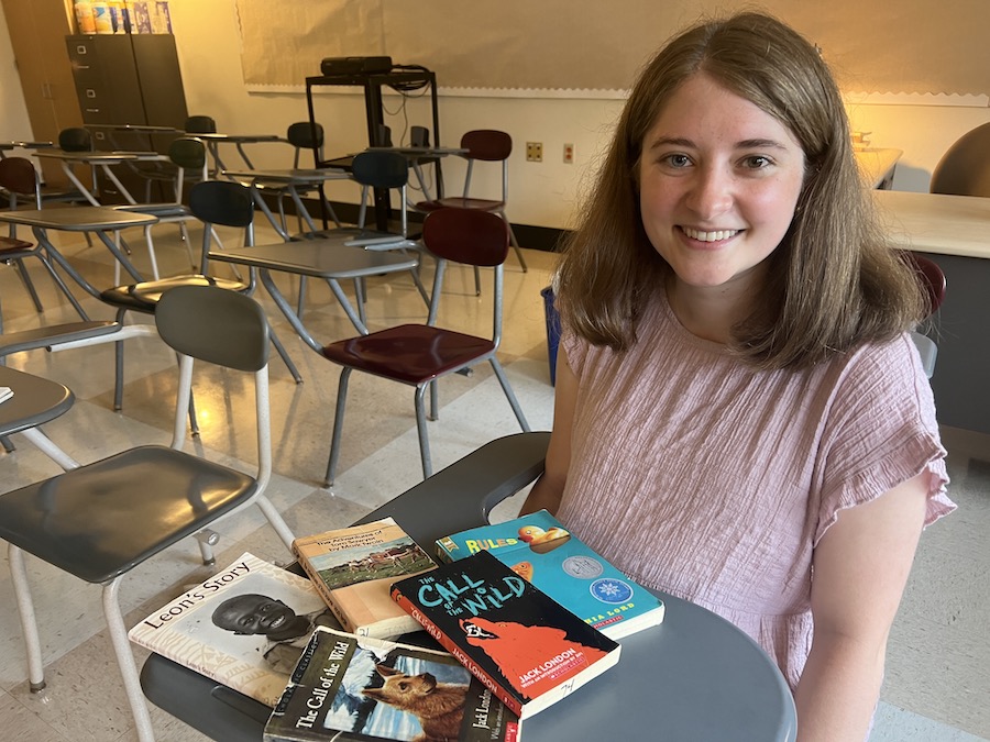 Taylor Jorgensen Emery ’22 sitting in her class with the books she'll teach in front of her