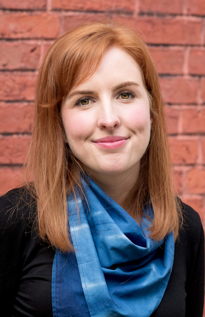 A headshot of a smiling person with a blue scarf
