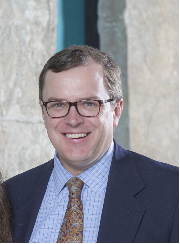 A headshot of a smiling person wearing glasses and a tie