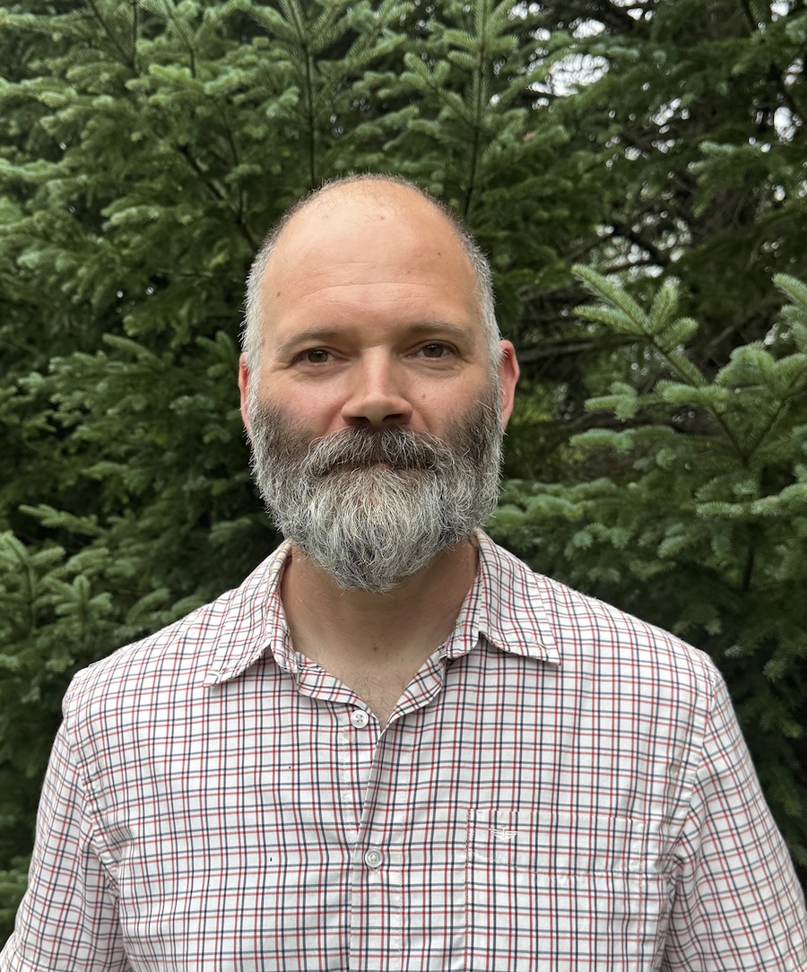 A headshot of a smiling person standing in front of trees